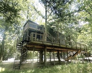 Uma casa na árvore com deck de madeira, escada e guarda-corpo de metal.