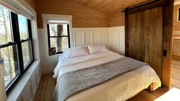 A bedroom with a bed, a window, and a wooden ceiling.