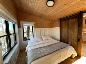 Un dormitorio con cama, ventana y techo de madera.