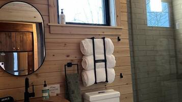 A bathroom with wooden walls, a window, a mirror, a sink, a toilet, and a shower area.