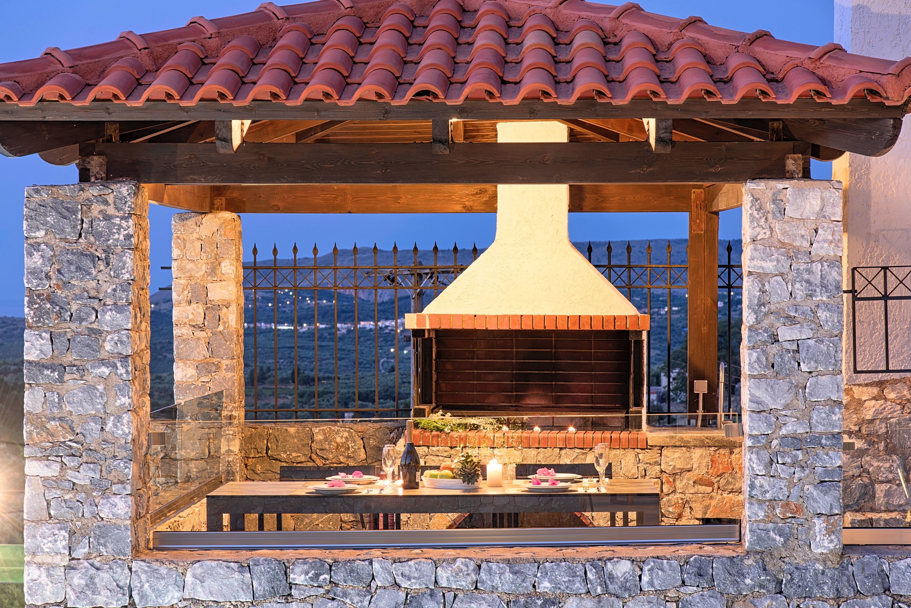 An outdoor dining area with a stone wall and a brick chimney, overlooking a mountainous landscape.