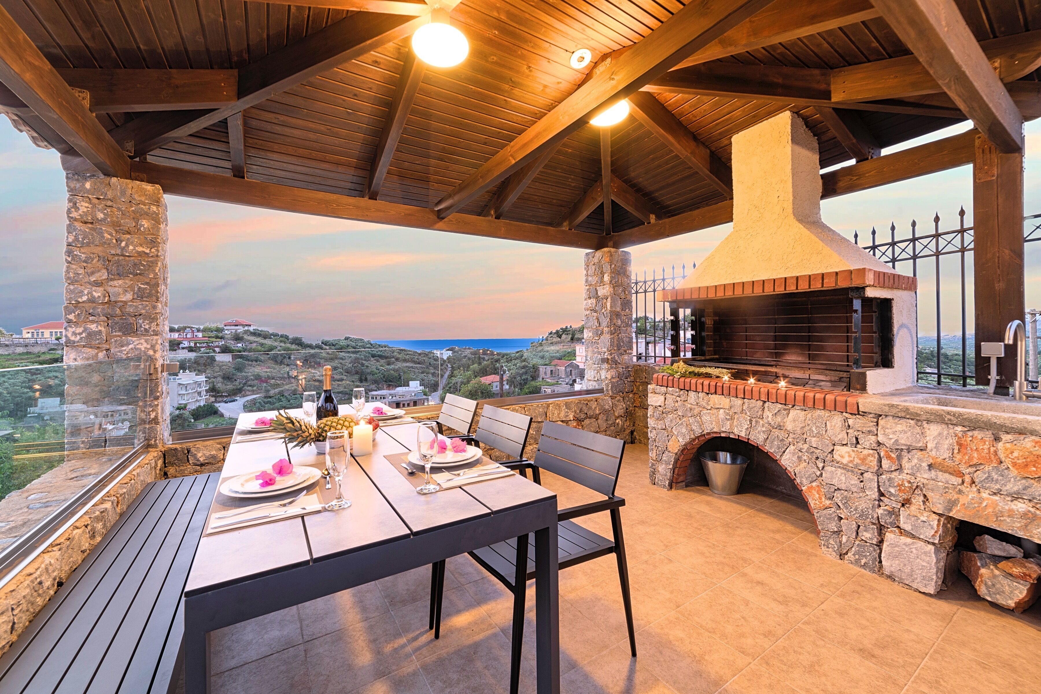 An outdoor dining area with a stone fireplace, wooden ceiling, and a view of the landscape.