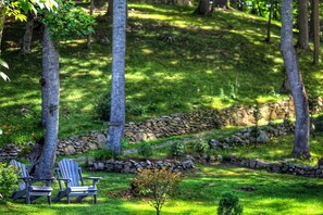 A grassy outdoor area with Adirondack chairs, a stone wall, and trees. - Incredible Secluded Barn with Hot-tub and Petting Zoo in Sugar Grove, North Carolina (Sugar Grove)