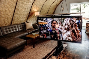 Ein Wohnzimmer mit einem großen Flachbildfernseher, einem Ledersofa, einem Couchtisch und einem gewebten Teppich.