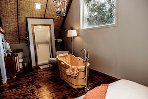 A room with a wooden bathtub, a door leading to a bathroom, a window with a view of trees, and a chandelier. - Incredible Secluded Barn with Hot-tub and Petting Zoo in Sugar Grove, North Carolina (Sugar Grove)