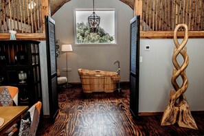 Ein Zimmer mit einer Holzwanne, einer Holzskulptur und einem Fenster mit Blick auf Bäume.