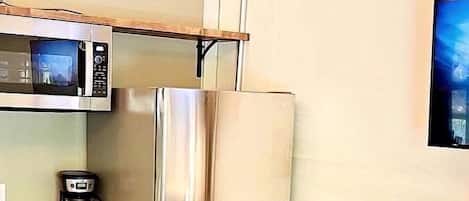 A compact kitchen with a microwave, refrigerator, coffee maker, and a wooden table.