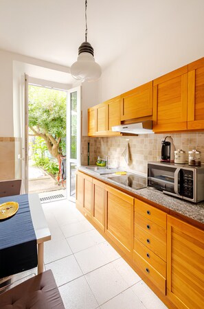 A modern kitchen with wooden cabinets, a built-in microwave, and a window overlooking a garden. - [Liberty Square] Historic Apt for 8 - 4BR, Private Courtyard, 10 min to Duomo (Firenze)