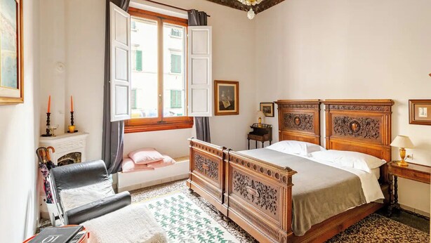 Un dormitorio con cama, una silla, chimenea y ventana con cortinas.