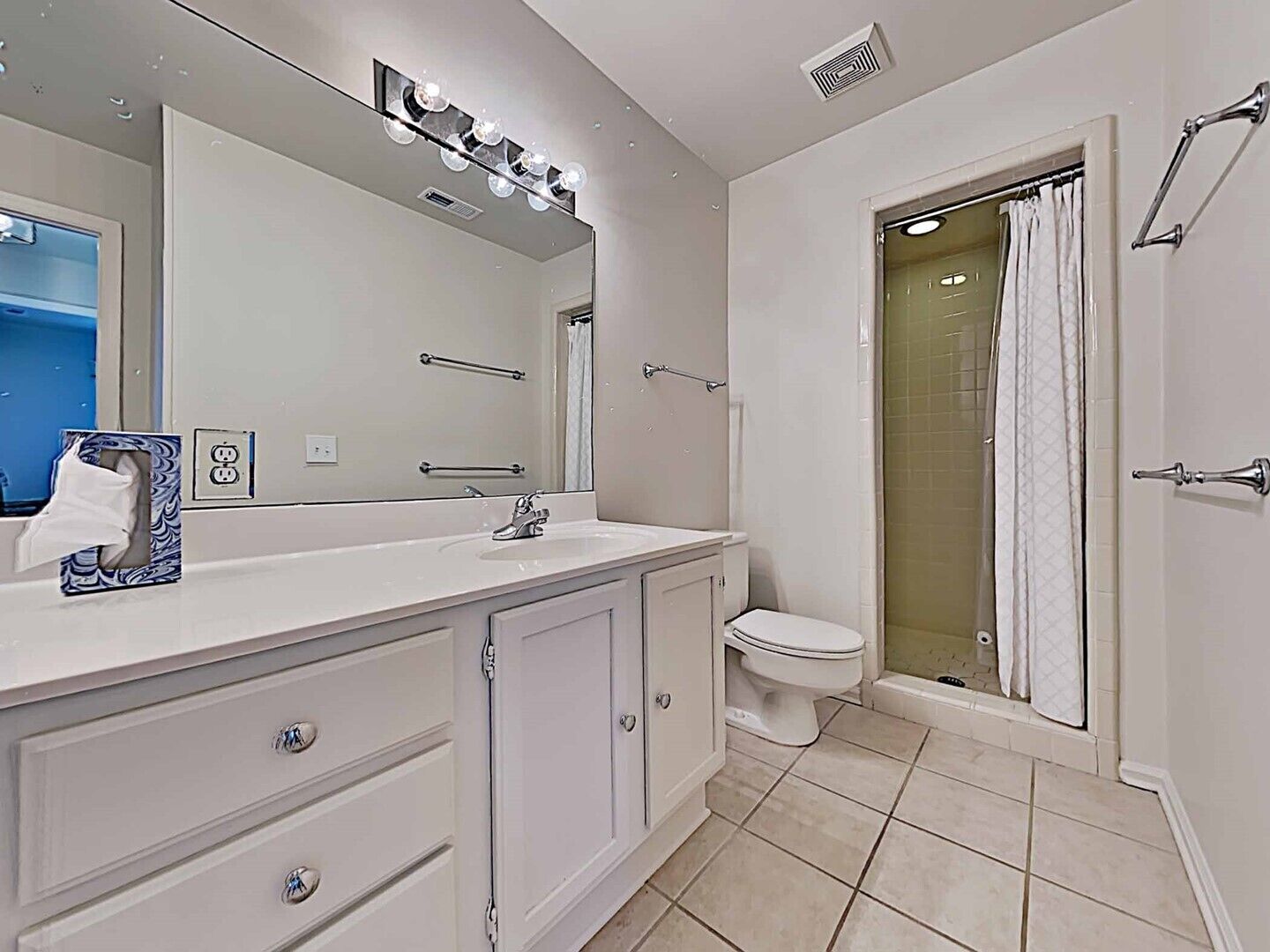 A bathroom with a white vanity, a mirror with lights, a toilet, and a shower area.
