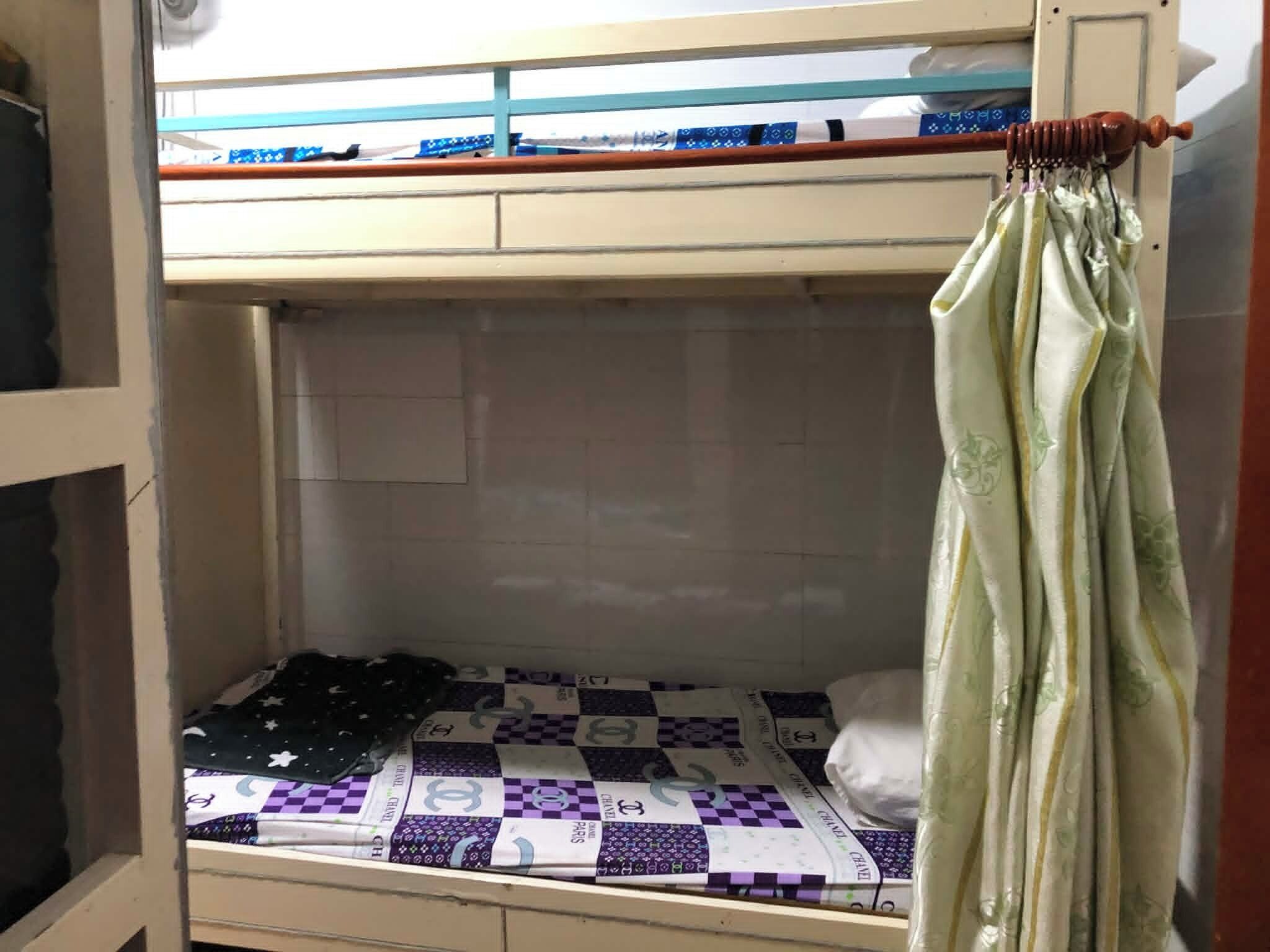 A bunk bed with a checkered bedspread, a curtain, and a window with blinds.