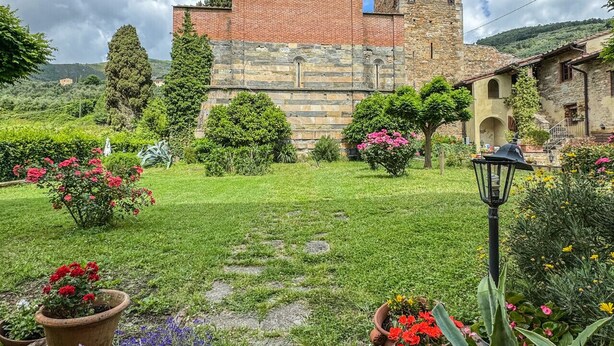 En historisk byggnad med ett klocktorn, omgiven av en välskött trädgård med olika växter och blommor.