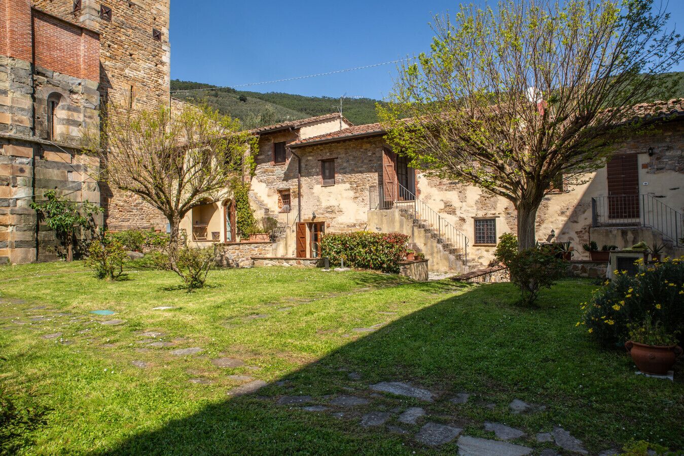 Un patio con edificios de piedra, un árbol y una zona verde.