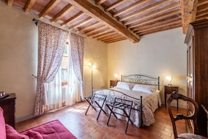 Um quarto com uma cama, uma cadeira, uma mesa de cabeceira e uma janela com cortinas.