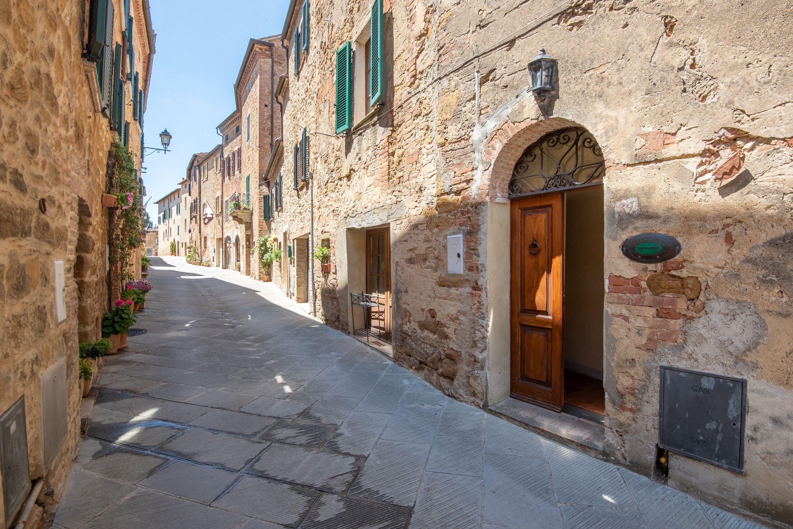 A narrow street with stone buildings, wooden doors, and a clear sky.