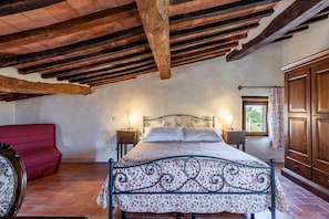 Ein Schlafzimmer mit einem Bett, Holzbalken, einem roten Sofa und einem Fenster mit Vorhängen.