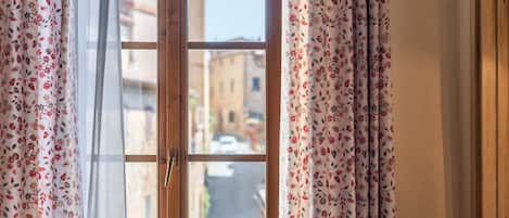 A window with floral curtains, a view of a street, and a building in the background.