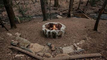 A campfire in a forest clearing surrounded by rocks and trees.