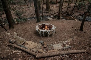 A campfire in a forest clearing surrounded by rocks and trees. - Chic Falls-Side Family Getaway: Dome Stay in Cherry Log, Georgia (Cherry Log)