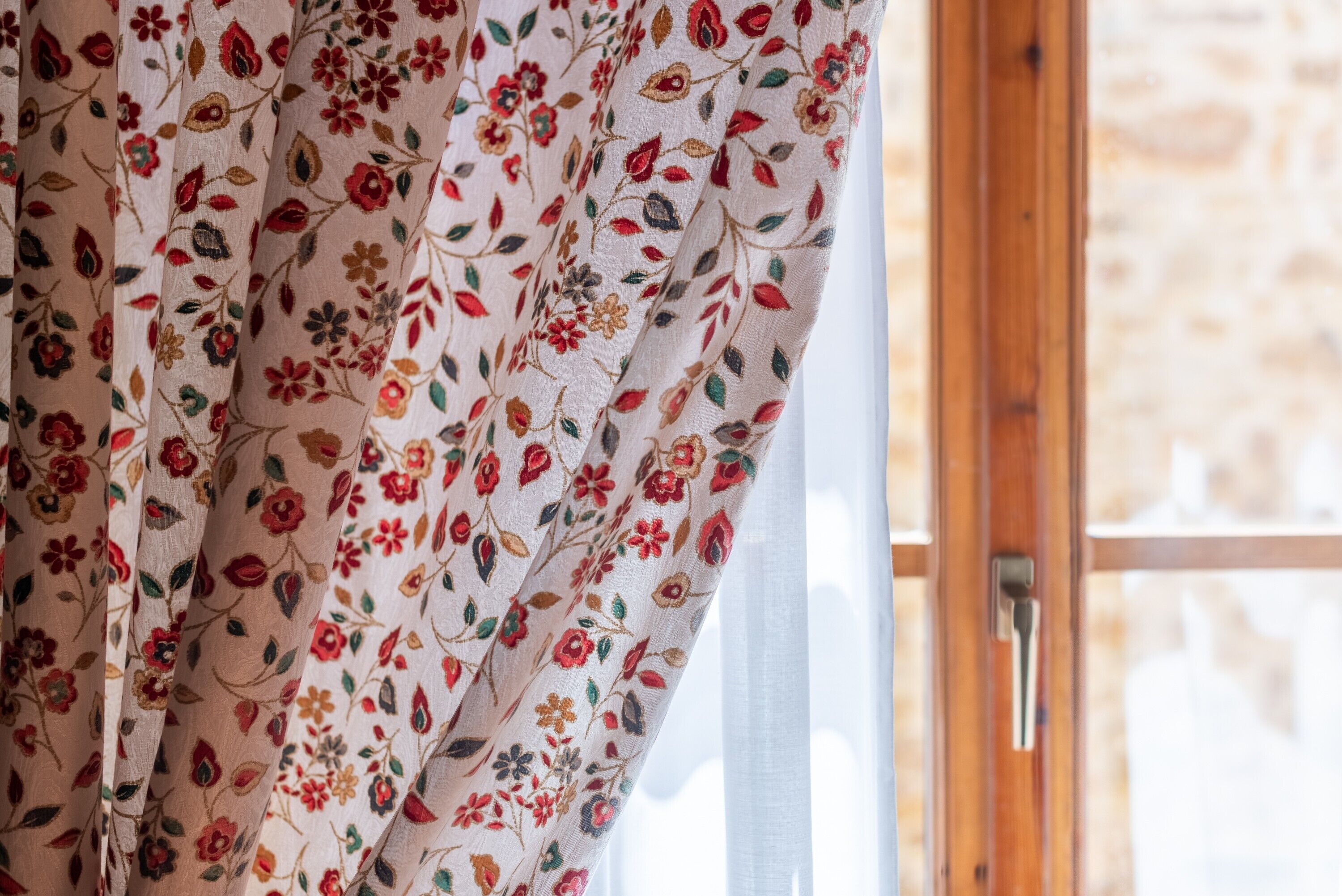 Ein Fenster mit Holzrahmen und Vorhang mit Blumenmuster.