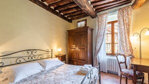 A bedroom with a bed, wooden wardrobe, chair, and a window with curtains.