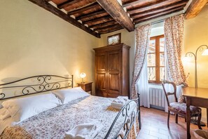 Une chambre à coucher avec un lit, une armoire en bois, une chaise et une fenêtre avec des rideaux.