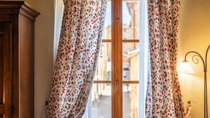 A window with floral curtains, a wooden door, and a wall-mounted lamp.