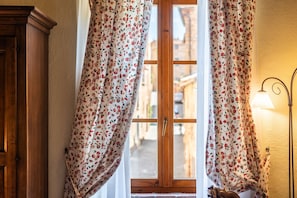 A window with floral curtains, a wooden door, and a wall-mounted lamp. - Locanda di Montisi Piazza Room between the hills of Montalcino (Montisi)