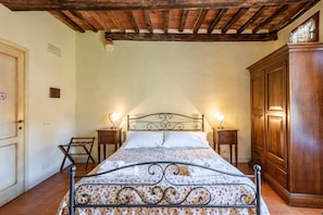 A bedroom with a bed, wooden wardrobe, two bedside tables with lamps, a chair, and a door with a sign. - Locanda di Montisi Piazza Room between the hills of Montalcino (Montisi)