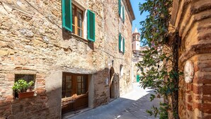 A narrow street with stone buildings, wooden shutters, and a bell tower in the distance.