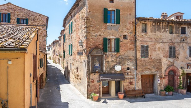 A narrow street with historic buildings, a bench, and a sign for 'La Lega di Montis.'
