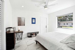 Un dormitorio con una cama, un escritorio, una silla, una ventana y un ventilador de techo.