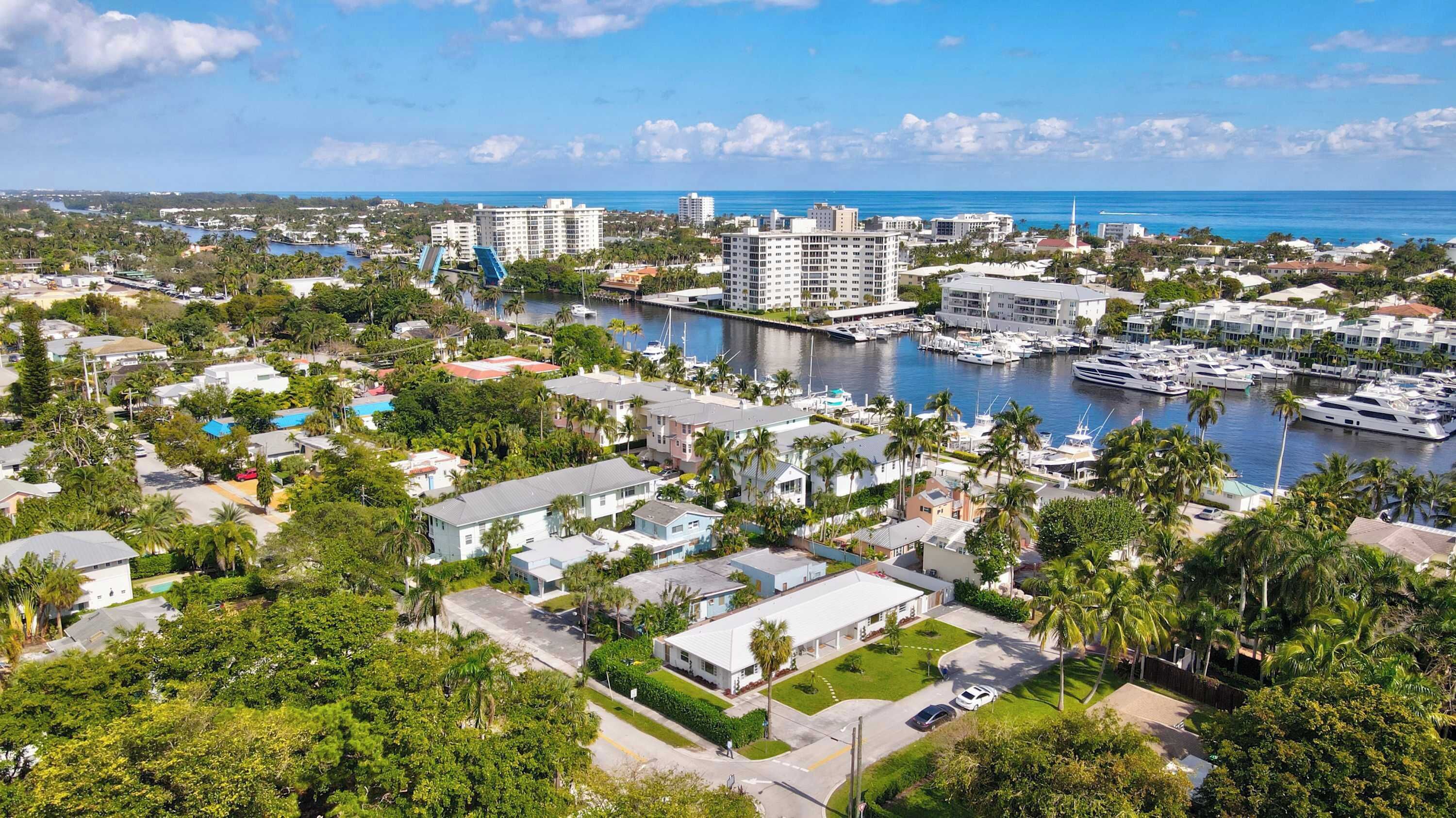 A marina with boats, a marina building, and residential buildings with palm trees.