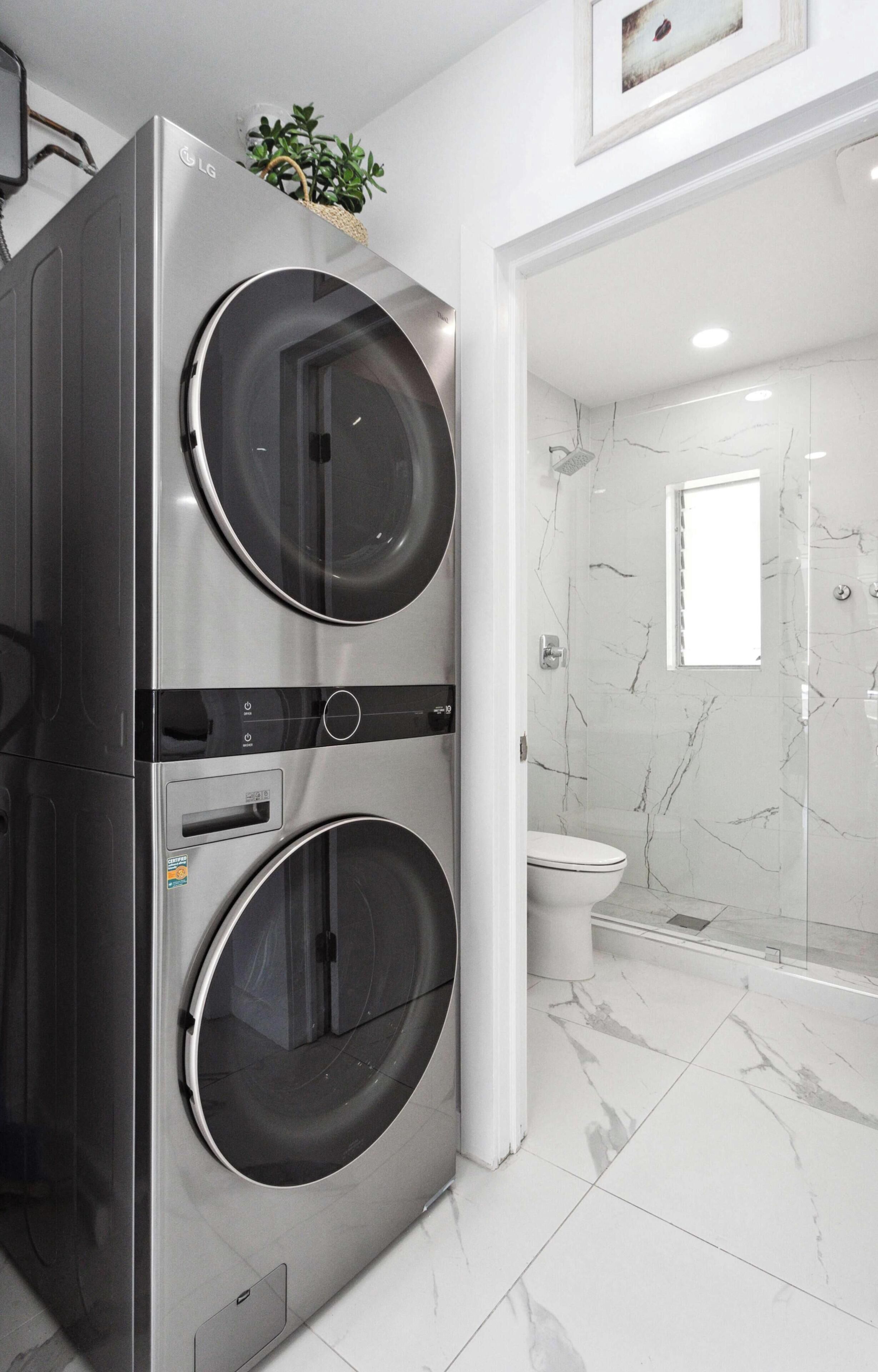 Un baño moderno con lavadora-secadora de acero inoxidable doble, inodoro y mampara de cristal para la ducha.