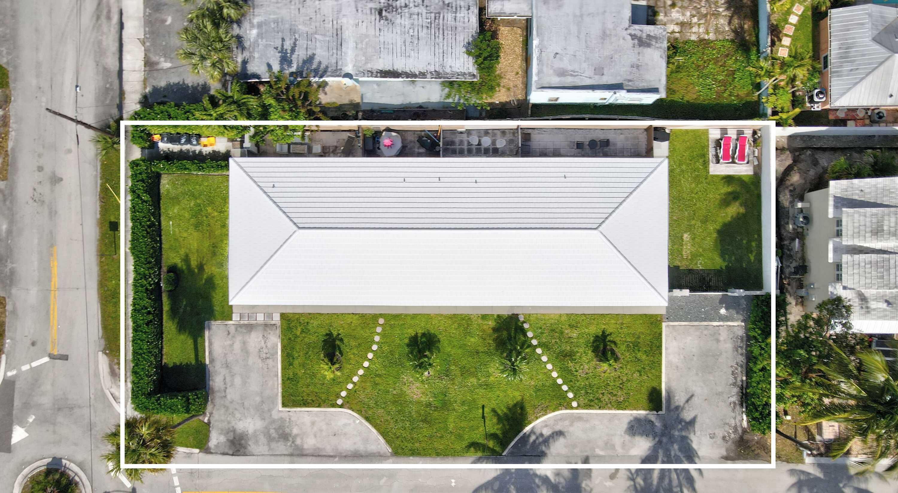 Vista aérea de un edificio con techo plano, rodeado de vegetación y una zona pavimentada.