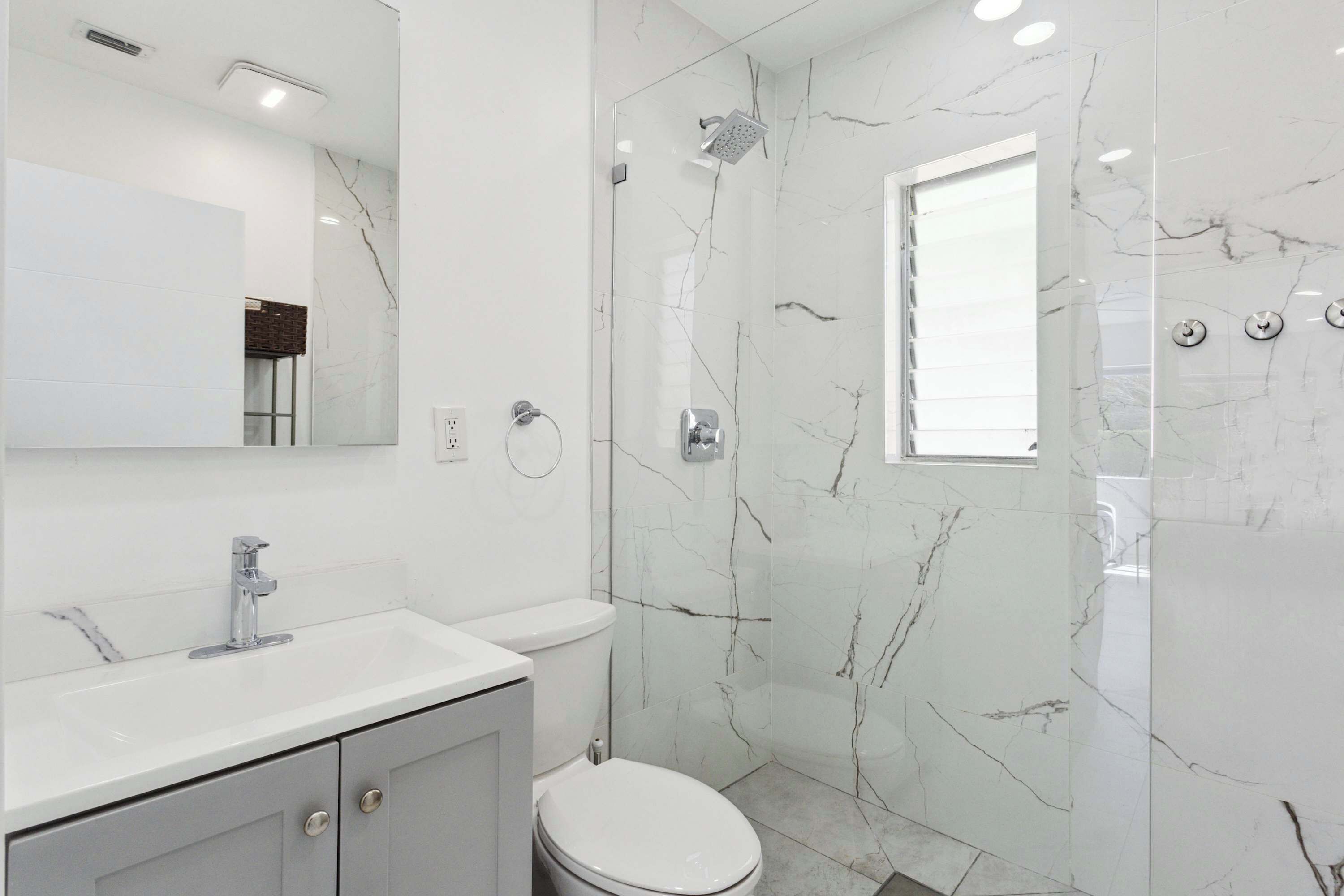 A modern bathroom with a white marble shower, a sink, and a toilet.