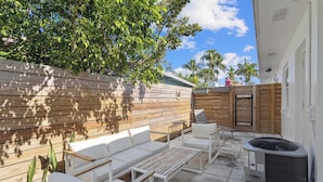 En terrasse med hvide møbler, et træhegn og en klimaanlæg.