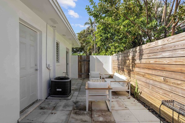 A patio with outdoor furniture, a trash can, and a wooden fence.