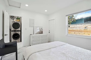 Un dormitorio con cama, cómoda, lavadora y ventana con vista a una cerca de madera.