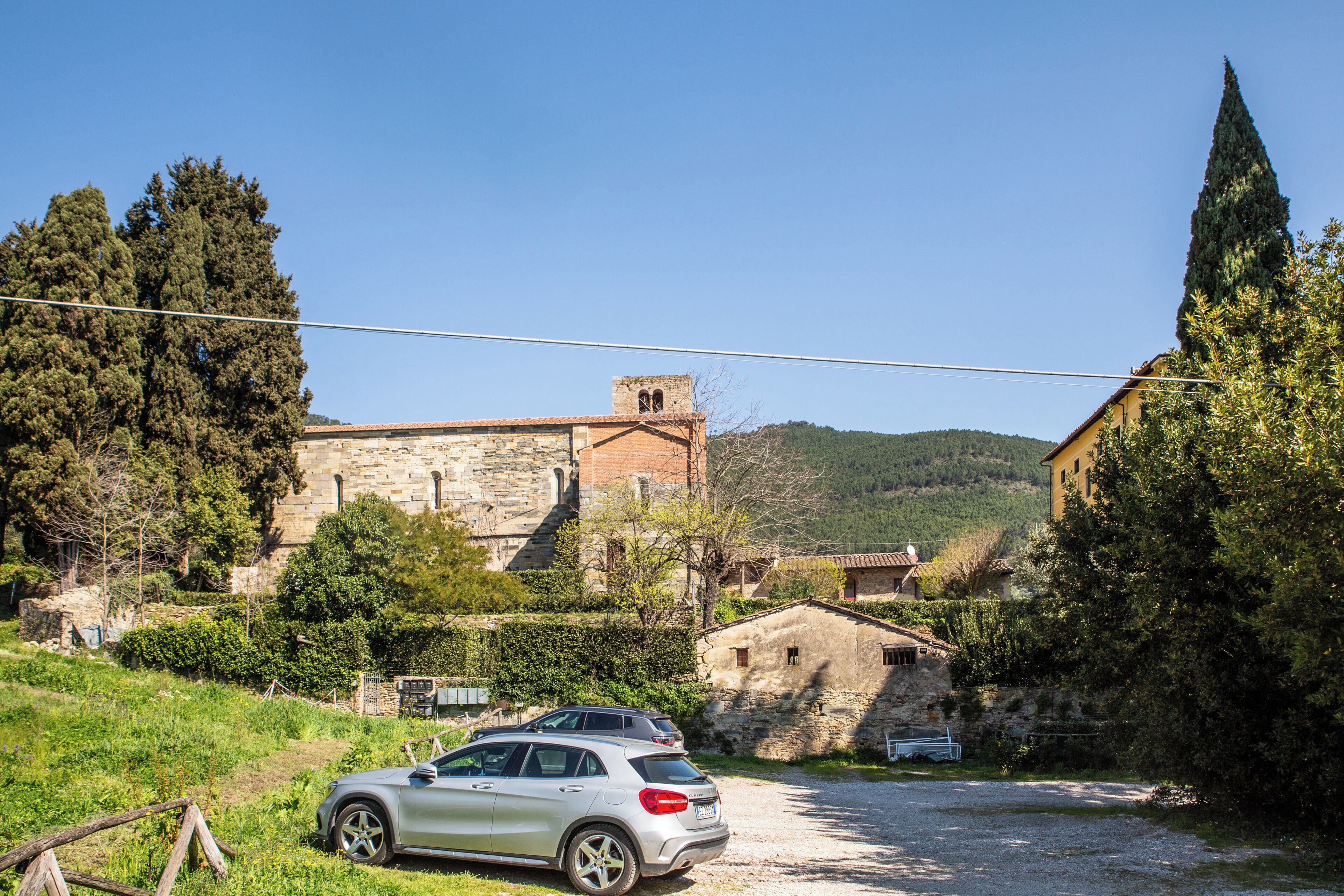 A rural setting with a stone building, a parked car, and a clear sky.