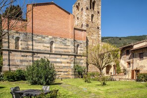 A stone building with a tower, a grassy courtyard, and a small outdoor seating area. - Borgo San Jacopo - Il Cipressino (Vicopisano)