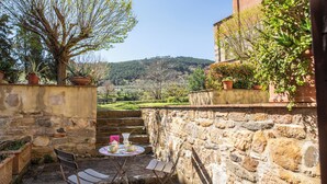 A stone-walled outdoor seating area with a table and chairs, surrounded by potted plants and a view of a hilly landscape. - Borgo San Jacopo - Il Cipressino (Vicopisano)