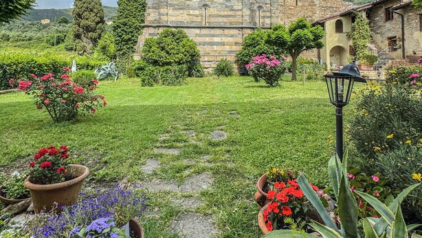 A historic building with a prominent tower, surrounded by a well-maintained garden with various flowering plants and a stone pathway. - Borgo San Jacopo - Il Cipressino (Vicopisano)
