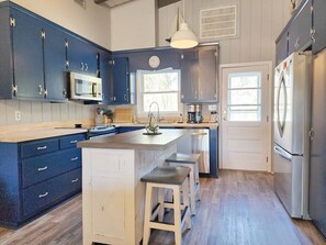 A modern kitchen with dark blue cabinets, a stainless steel refrigerator, and a central island with stools. - Beach Haven South - Minutes from the Beach, Second Row North Litchfield (Pawleys Island)