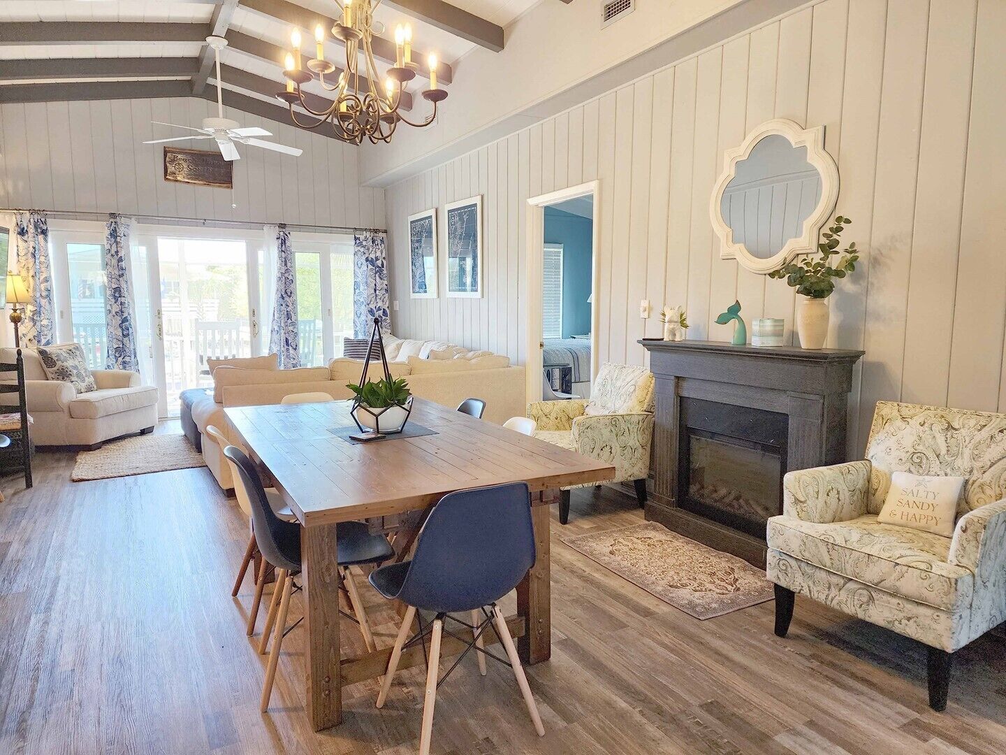 A spacious living room with a wooden dining table, comfortable seating, a fireplace, and a large mirror on the wall.