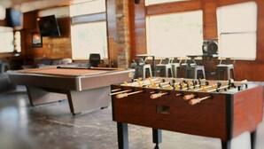 Una taula de bitlles i una taula de futbolí en una habitació amb grans finestres i una paret de maó.