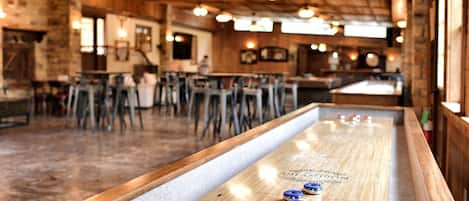 A bar area with a shuffleboard table, wooden ceiling, and bar stools.