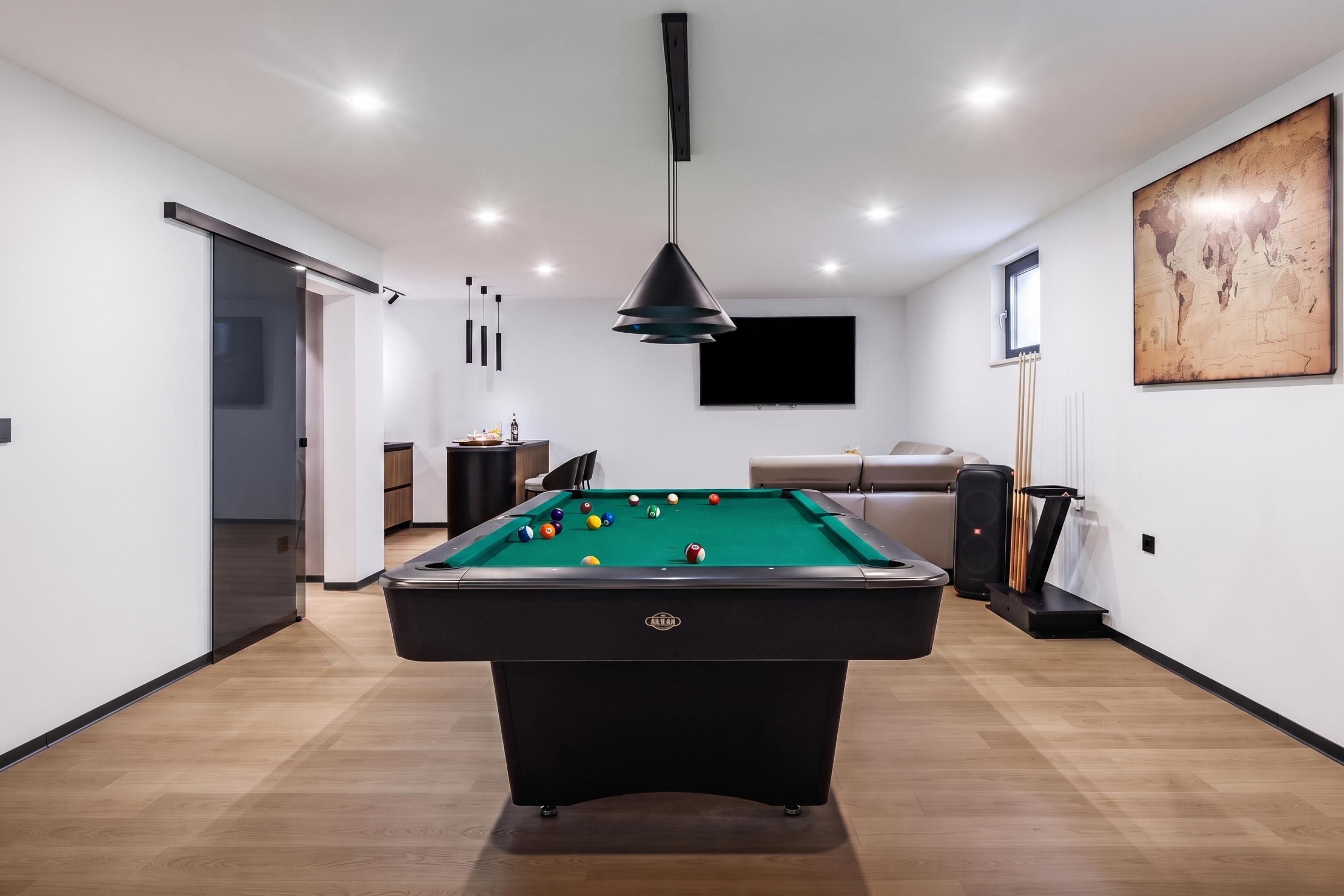 Una habitación moderna con mesa de billar, sofá y televisor.
