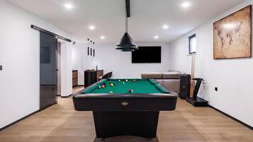 Una habitación moderna con mesa de billar, sofá y televisor.