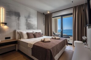 Une chambre d’hôtel moderne avec un grand lit, une table de chevet, une petite table avec une chaise et une vue sur la mer.